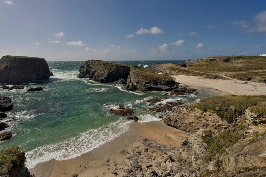A coastal landscape with rocky cliffs, a sandy beach, and the ocean. 2