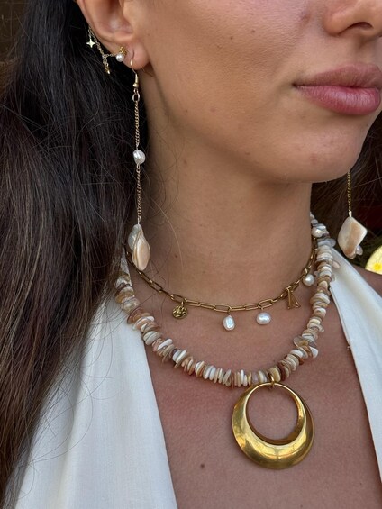 A person wearing a white top, a gold necklace with a circular pendant, and pearl earrings. 4