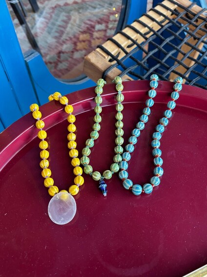 Three necklaces with beads in yellow, green, and blue colors, and a pendant on the left. 1