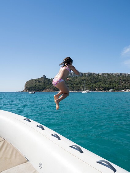 A person jumping off a boat into turquoise water with a coastal landscape in the background. 4