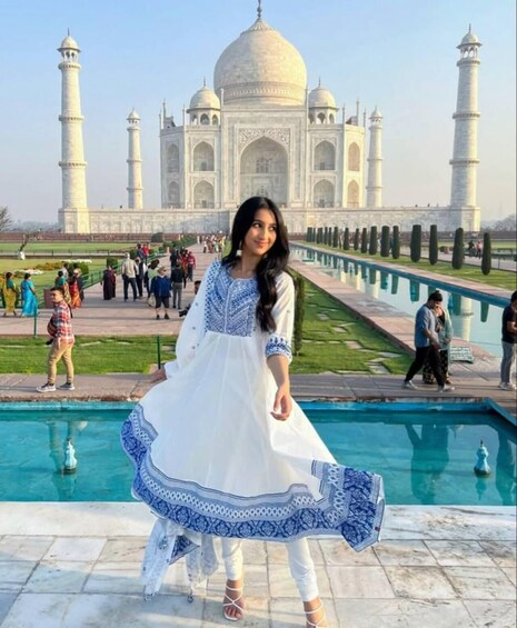 A person in a white dress with blue patterns standing in front of the Taj Mahal. 5