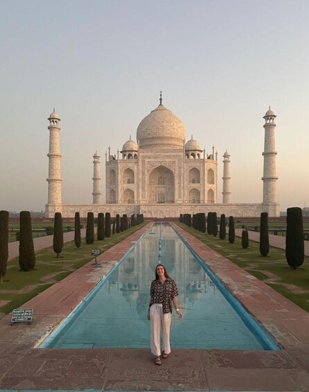 A person standing in front of the Taj Mahal with a clear reflection in the pool. 2