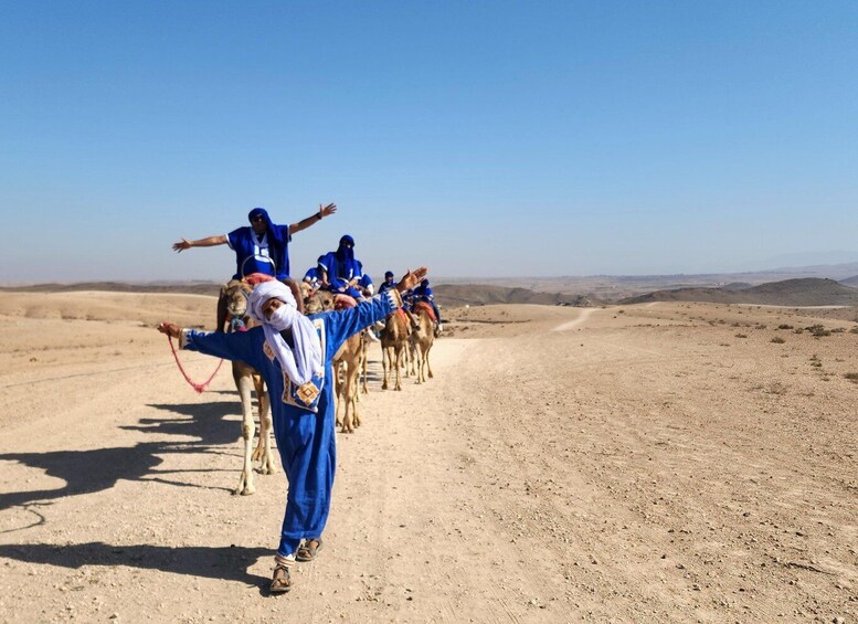 A group of people in blue attire leading camels across a desert landscape. 1