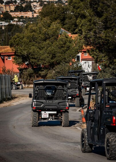 A convoy of off-road vehicles on a road with houses and trees in the background. 2
