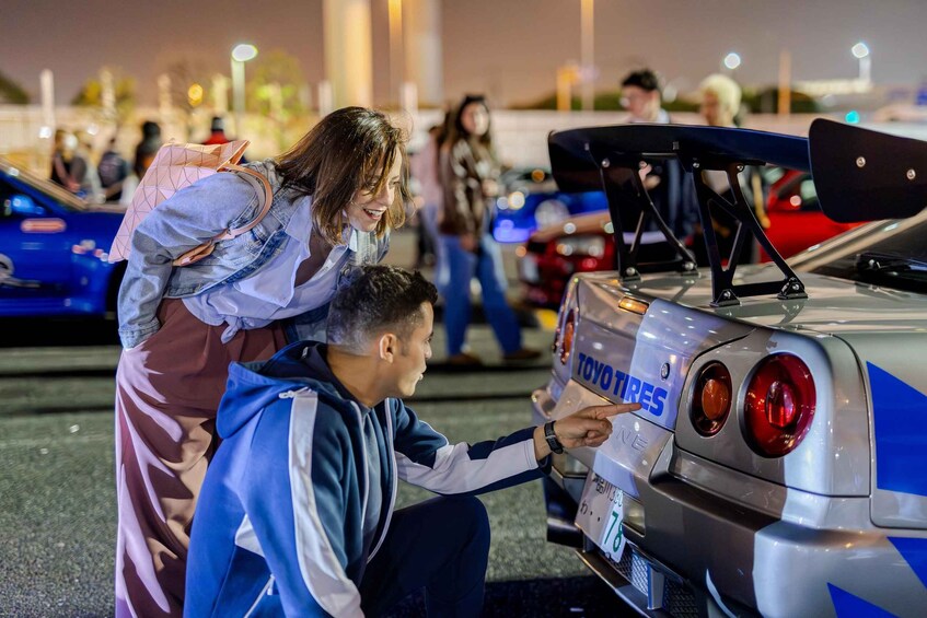 A person pointing at a car with a license plate and a 'TOYO TIRES' decal. 1