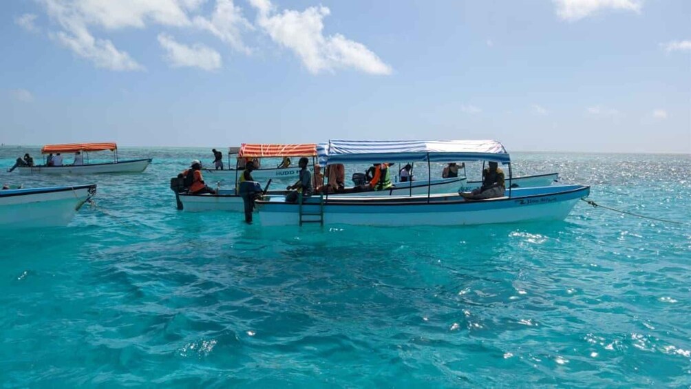 A clear blue sea with several boats, some with canopies, and a few people on board. 2