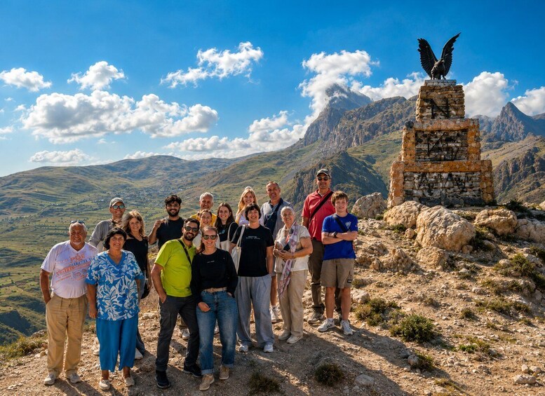 A group of people standing on a rocky outcrop with a mountain range in the background and a stone monument with an eagle statue. 3
