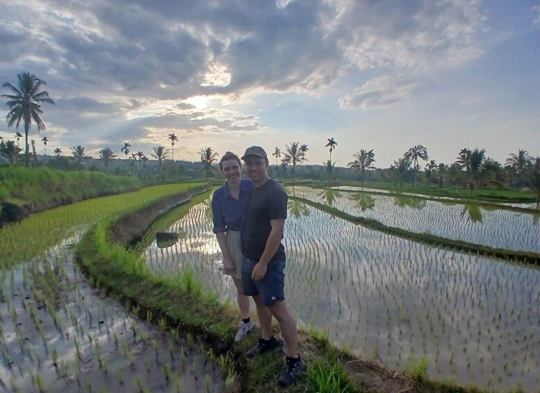 Two people standing in a rice paddy field with palm trees in the background. 2