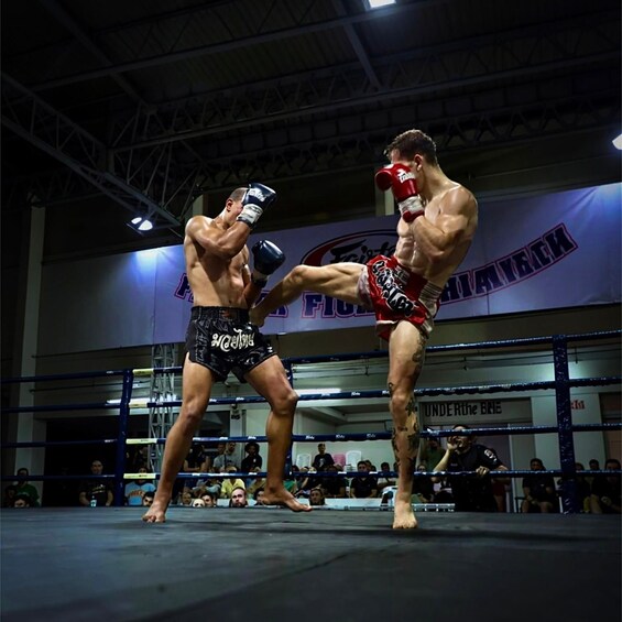 Two fighters in a boxing ring, one delivering a high kick. 1