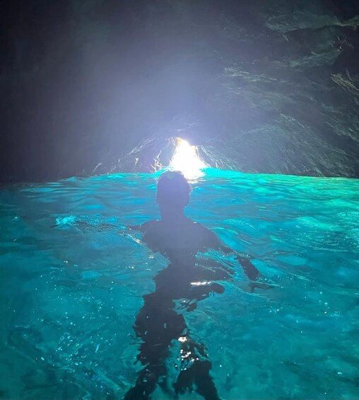 A person swimming in clear blue water with sunlight filtering through a cave entrance. 1