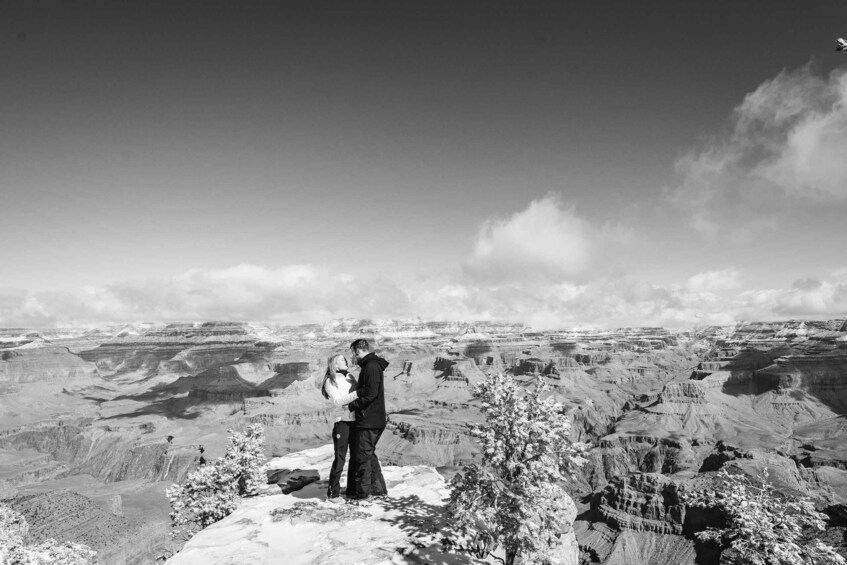 A couple kissing on a snowy mountain overlooking a vast canyon landscape. 5