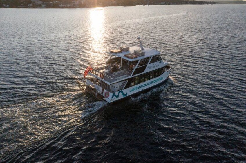 A white boat with "LAKEMACQUARIECRUISES" written on the side, moving on the water. 2