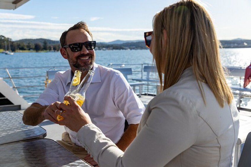 Two people sitting at a table by a body of water, holding drinks. 1