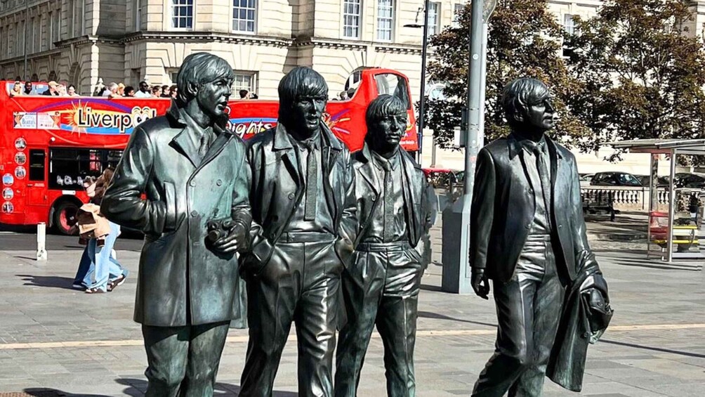 A statue of four figures in suits, a red bus, and a bus stop. 1