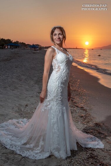 A woman in a white wedding dress standing on a beach at sunset. 3