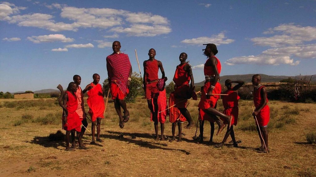 A group of people in red traditional attire walking across a dry grassland with a clear sky. 3