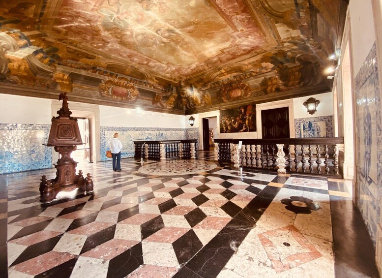 A grand hall with a checkered floor, ornate ceiling frescoes, and classical columns. 1