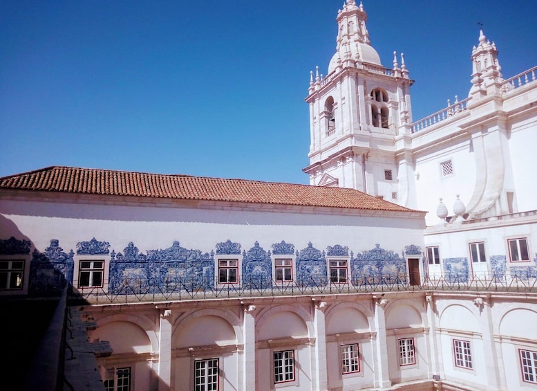 A historic building with white walls and blue decorative tiles, featuring a prominent bell tower and arched windows. 5