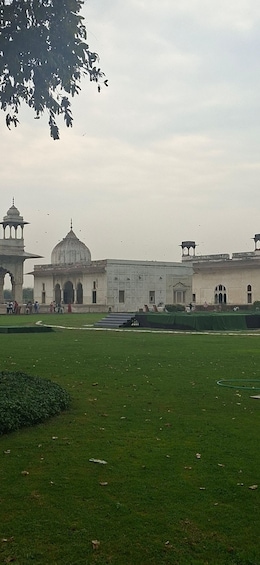 A large white building with a dome and minarets, surrounded by a green lawn and a few people walking. 4