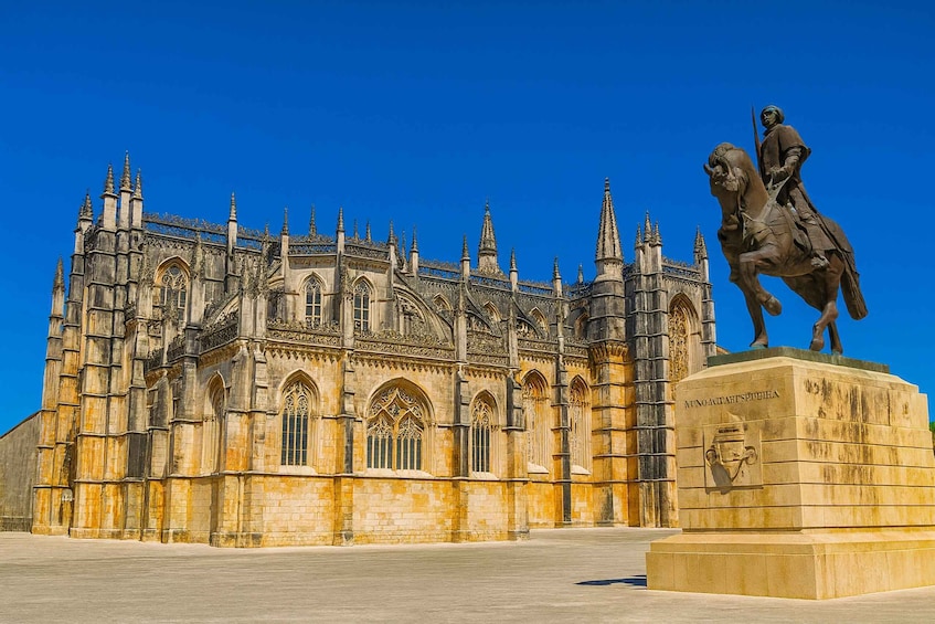 A historic cathedral with intricate Gothic architecture, a statue of a knight on horseback, and a clear blue sky. 2