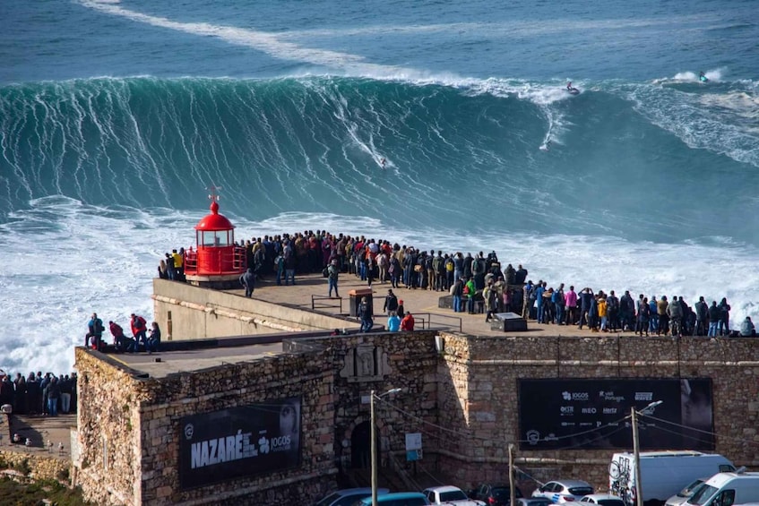 A coastal scene with a large crowd of people gathered on a stone platform overlooking the ocean, where surfers are riding waves. 1