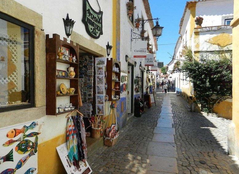 A narrow cobblestone street lined with shops displaying ceramics and paintings. 3