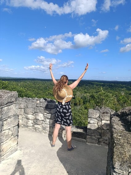 A person standing on a stone platform with arms raised, overlooking a lush green landscape. 4