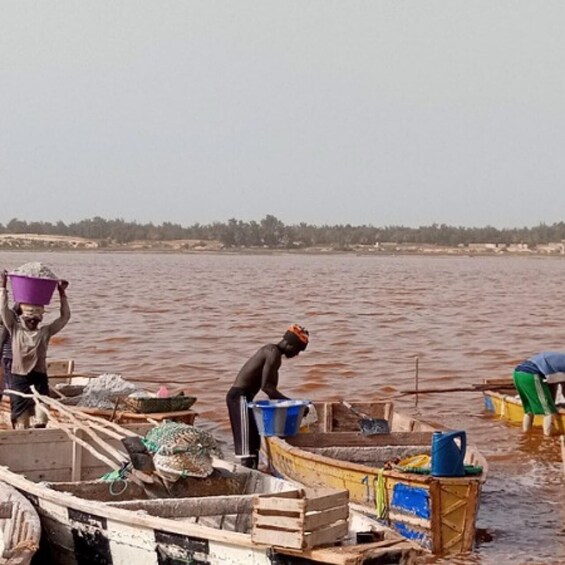People on a boat carrying buckets, with a river and distant trees in the background. 1