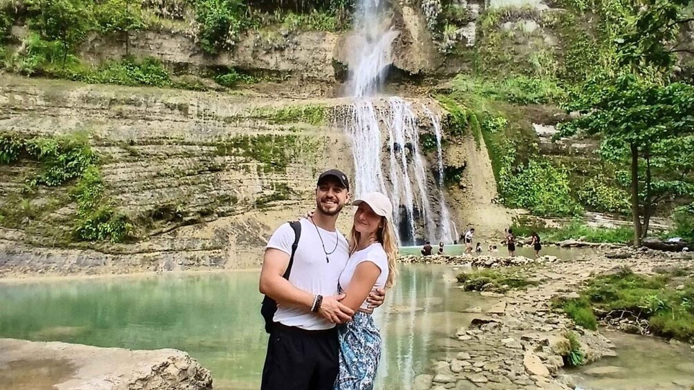 A couple embracing in front of a waterfall with a calm river and rocky terrain. 2