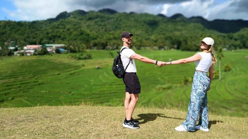 Two people holding hands on a grassy hill with a mountainous landscape in the background. 3