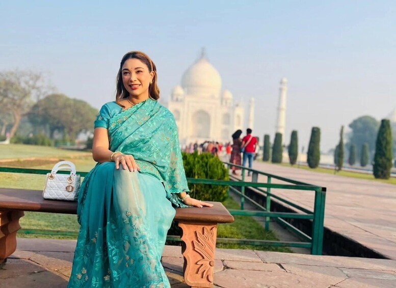 A person in a turquoise dress sitting on a bench with the Taj Mahal in the background. 4