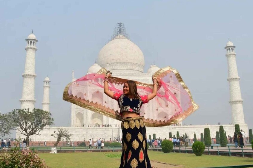 A person in traditional attire holding a large pink and gold cloth in front of the Taj Mahal. 3