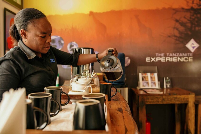 A person pouring coffee into a cup at a table with multiple coffee cups and a teapot. 2