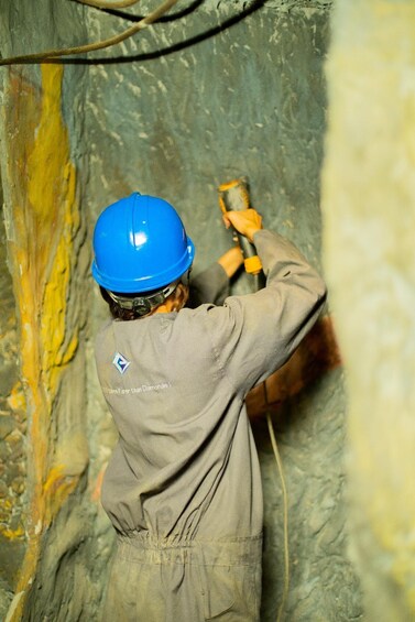 A person in a hard hat and work clothes using a tool in a cave. 4