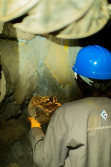 A person in a hard hat and work clothes examining a rock in a cave. 1