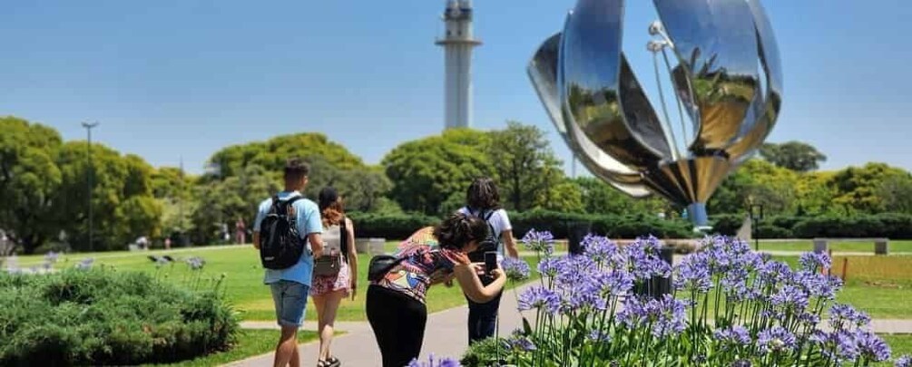 A park with a reflective sculpture, purple flowers, and a tower in the background. 2