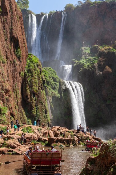A multi-tiered waterfall with people observing and a river with a wooden cart. 2
