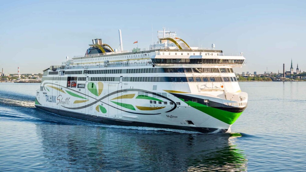 Un grand navire de croisière arborant les marques « TALINK Shuttle » et « MyStar », naviguant sur l’eau avec la silhouette d’une ville en arrière-plan. 1