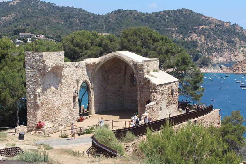 A stone structure with an arched doorway overlooking a coastal area with boats and a beach. 5