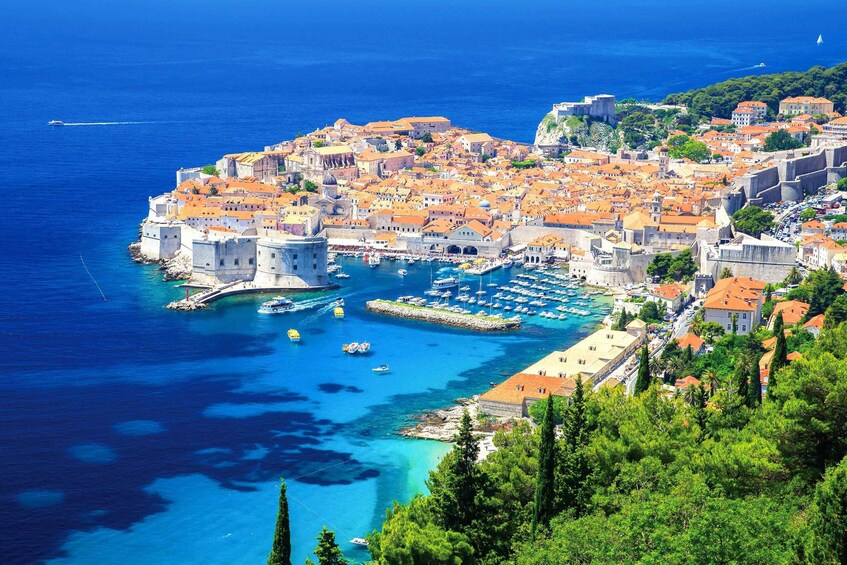 A coastal town with historic buildings, a harbor with boats, and a clear blue sea. 1