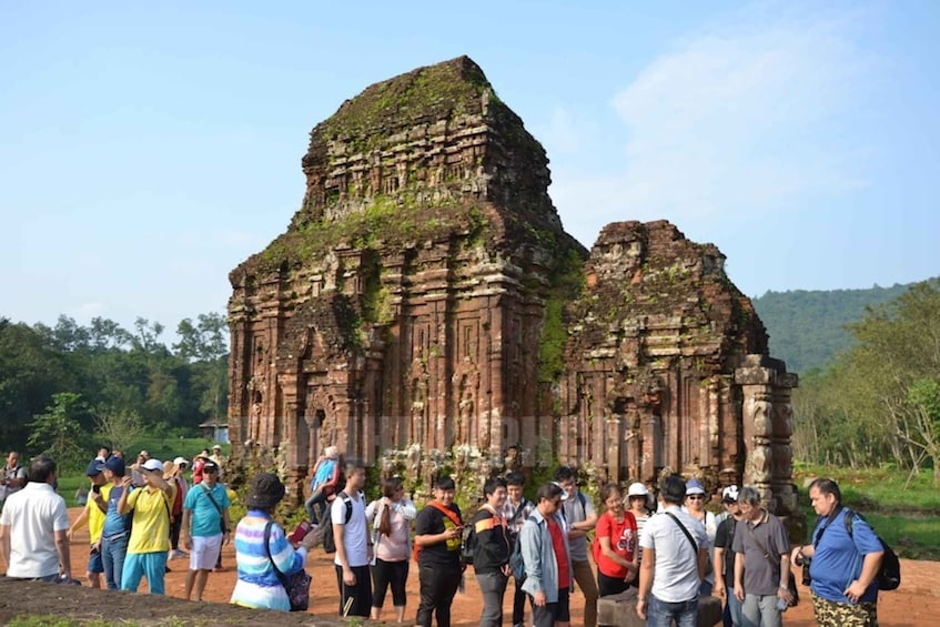 A group of tourists standing in front of ancient stone ruins with a forested background. 5
