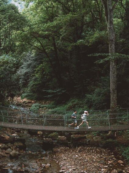 Two people running on a bridge over a stream in a forested area. 5