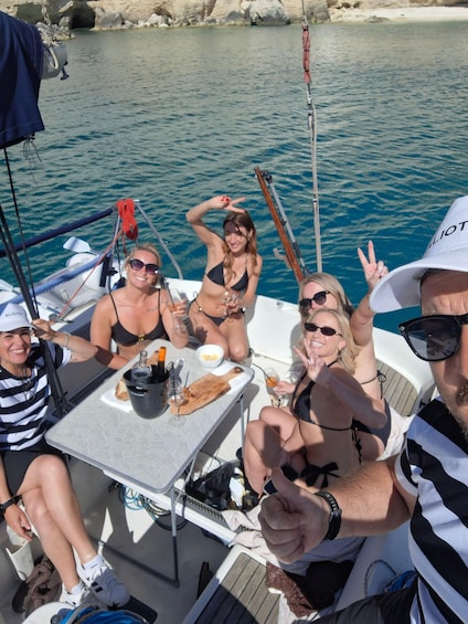 A group of people on a boat with a table set for a meal, surrounded by water and rocky terrain. 1