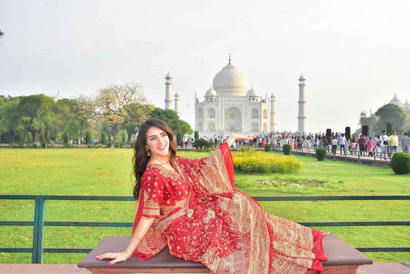 A person in a red traditional dress sitting on a bench with the Taj Mahal in the background. 4
