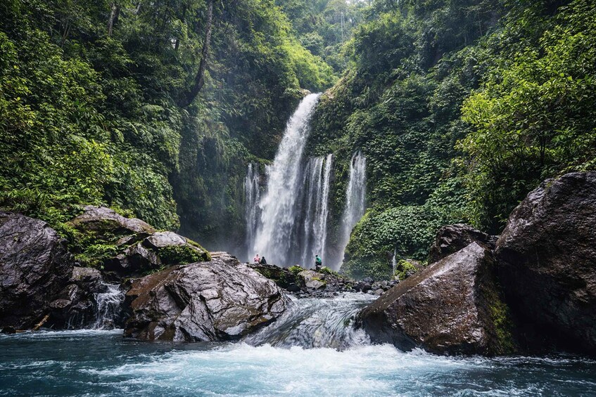 A multi-tiered waterfall surrounded by lush greenery and rocky terrain. 1
