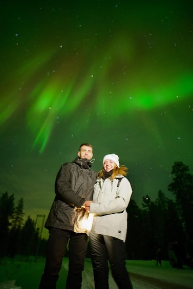 Two people standing under a green aurora display. 3