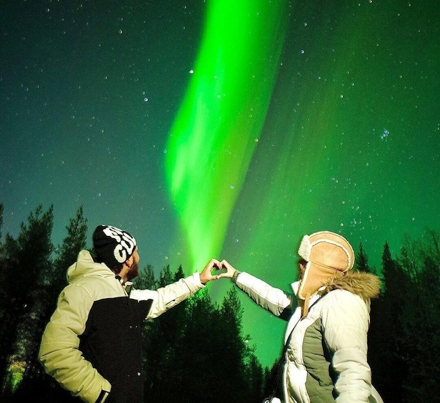 Two people making a heart shape with their hands under the aurora borealis. 1