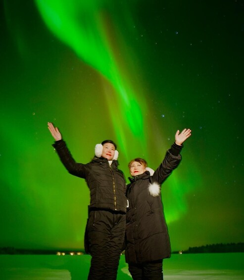 Two people standing with arms raised against a green aurora display. 5