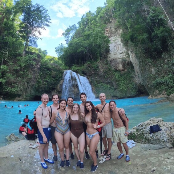 A group of people posing in front of a waterfall with a clear blue pool. 2