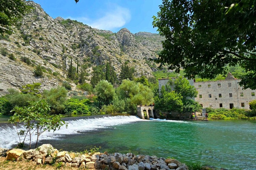 A river with a waterfall, a stone building, and a mountainous backdrop. 2